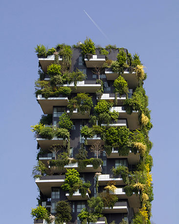 A tall, modern building, features numerous balconies densely populated with a variety of trees and greenery, set against a clear blue sky.